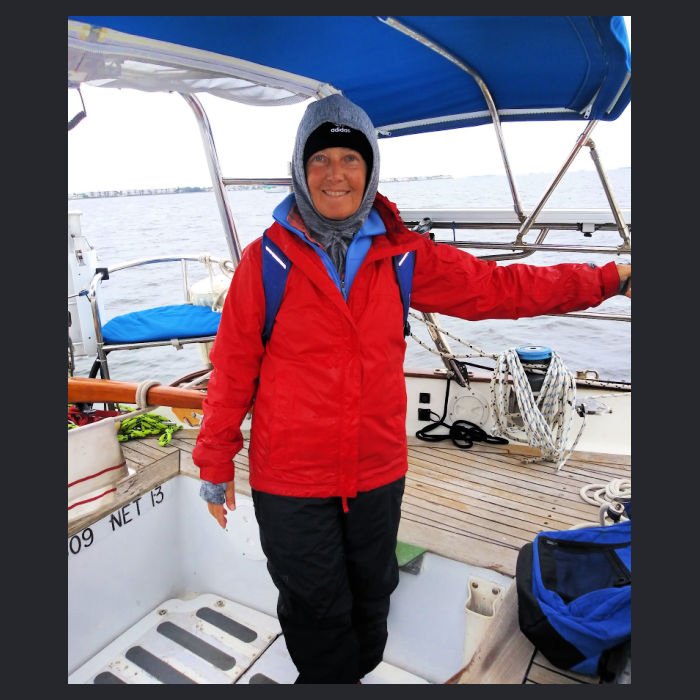 women in rain paints, rain jacket, hat and hood in cockpit of sailboat on cold FL day
