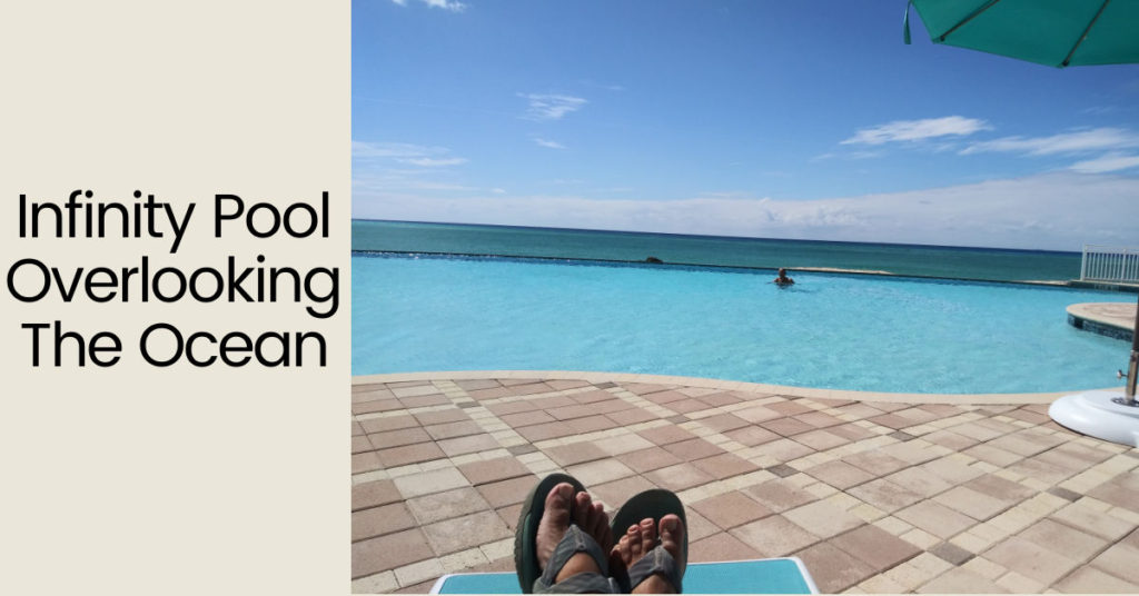 photo of feet on lounge chair on poolside and Tony in pool which overlooks the ocean 
