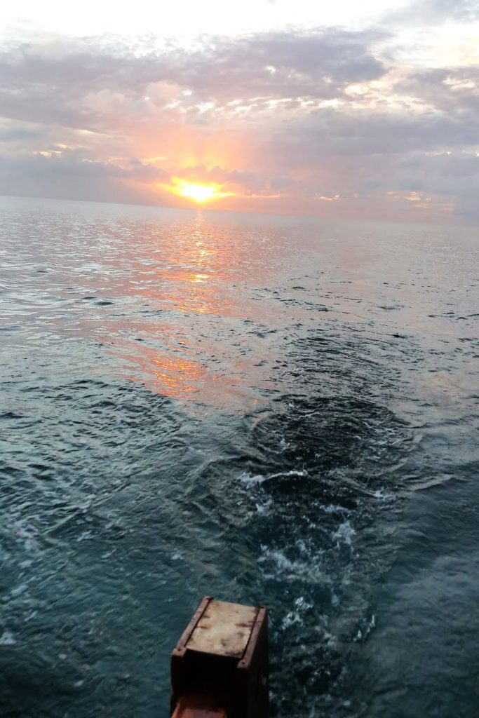 picture of water off stern of sailboat showing the sun setting 