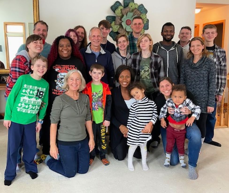 family picture of 21: parents, 6 adult kids, 9 grandchildren standing in a living room.