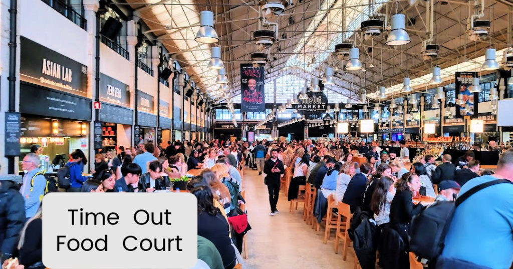 Inside a food court in Lisbon, people at long tables eating with restaurants surrounding the eating area “Time Out” food court