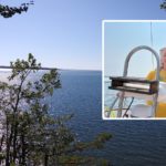 man and woman at wheel of sailboat, view of lake superior through the trees