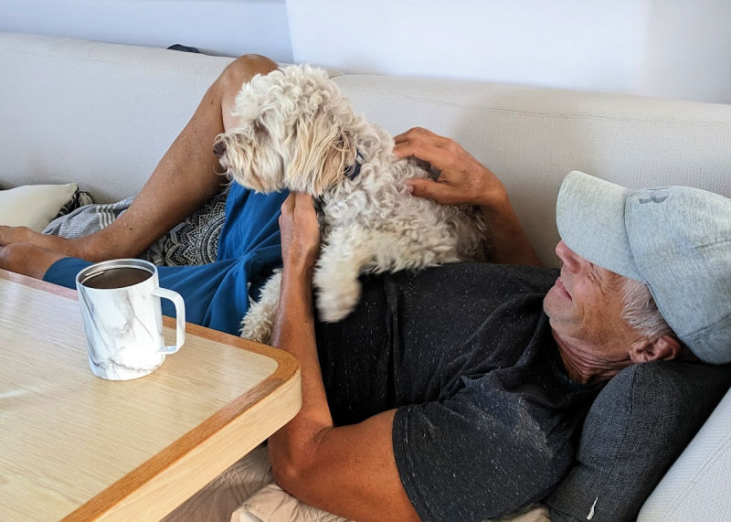 man resting on couch with dog on his lap 