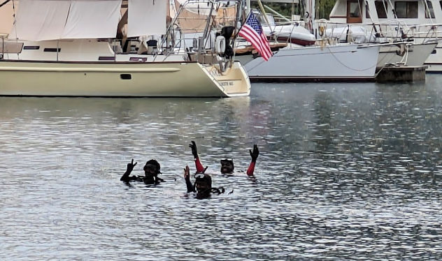 swimmers in the water by boats waving at the camera 
