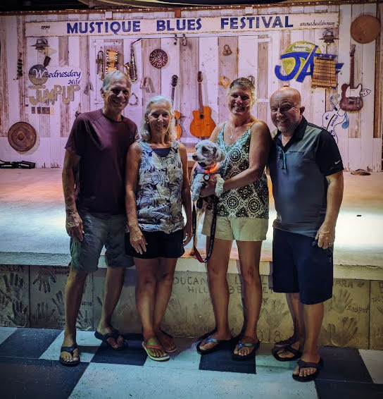 two couples with dog in front of Mustique Basil's Bar stage with musical instruments on the wall 