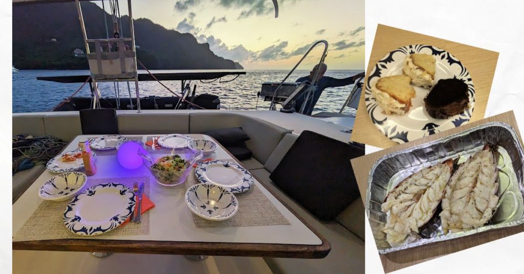 meal in cockpit with salad, lobster, coconut and chocolate cake with island in background 