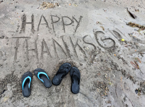 happy thanksgiving written in the sand with flip flops 
