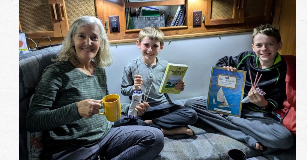 boys and grandma with hot cocoa, reading books and snack of pocky sticks in sailboat cabin 
