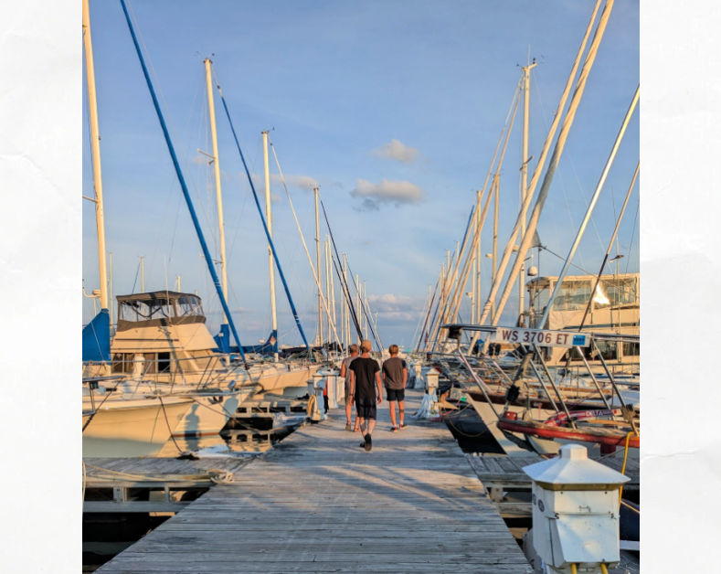 teens walking down marina dock with sailboats on either side 