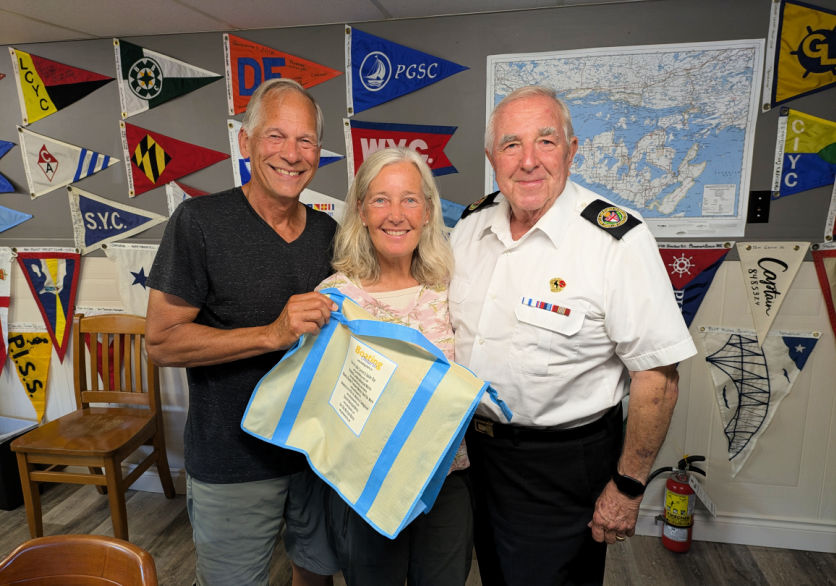 couple with Roy at Cruisers Net in Little Current, flags and charts on wall