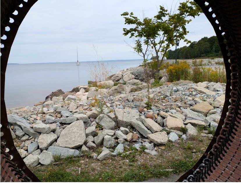 sailboat at anchor viewed from inside a metal wheel with rocks and trees in foreground