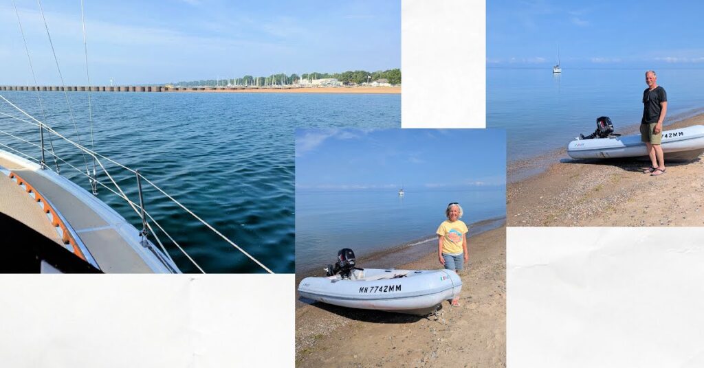 side of boat anchored off break water and beach with calm water, man and woman standing by dinghy on the shore with sailboat in distance 