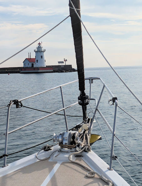 sailboat bow entering harbor beach harbor with picturesque lighthouse on breakwater 