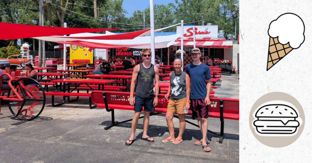 Restaurant and ice cream shop with picnic tables and awnings, grandma and teen grandsons near entrance 