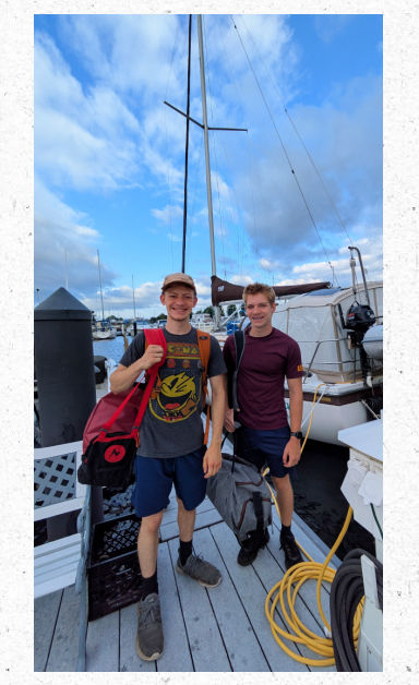 teen boys packed in duffel bags on dock of marina sailboat in background 