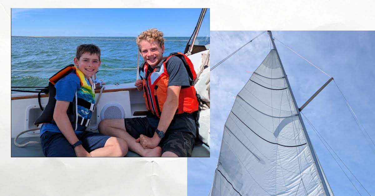 boys in lifejackets in cockpit of sailboat, reefed mainsail full of wind with blue sky