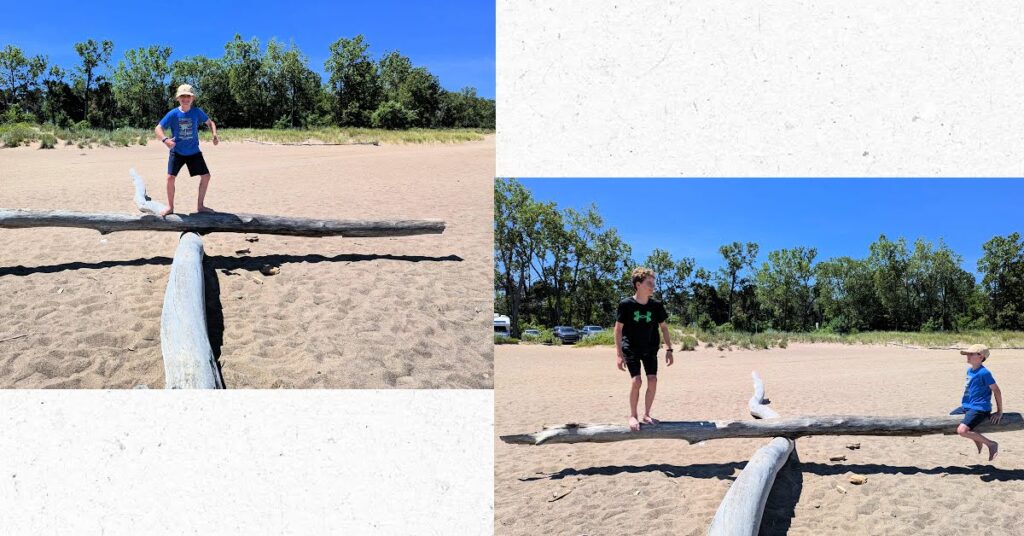 boys standing on a balanced log at beach 
