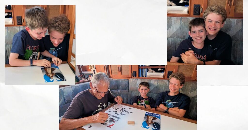 grandsons and grandpa doing a jigsaw puzzle competition in sailboat cabin at the dining table 
