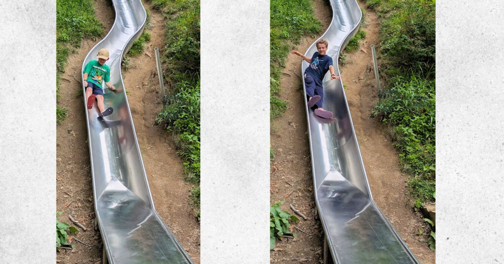 boys riding down metal slides built into hill 