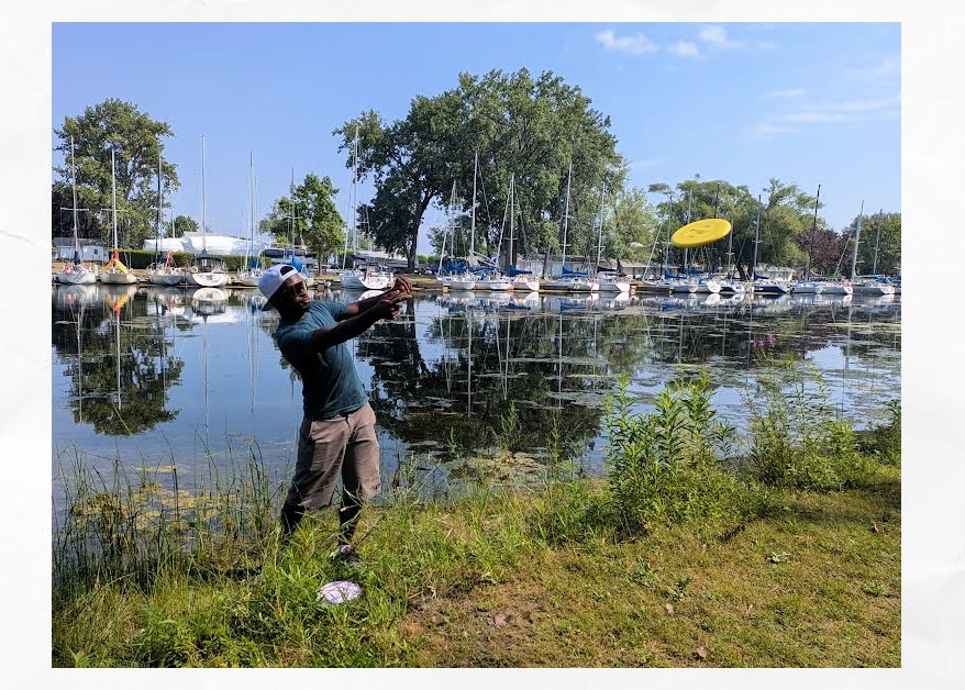 man throwing disc golf with sailboats in background
