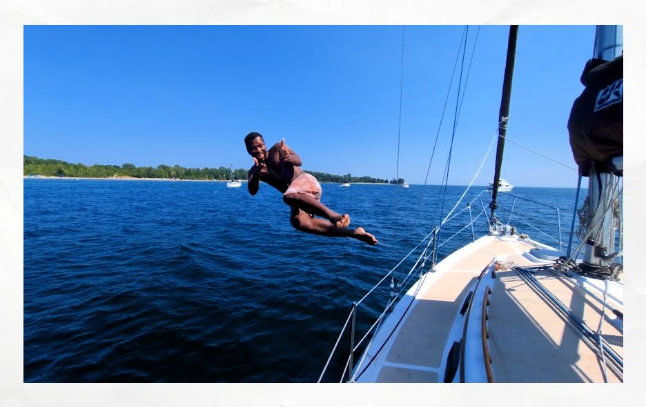 young man jumping off sailboat for a swim and making a thumbs up pose 