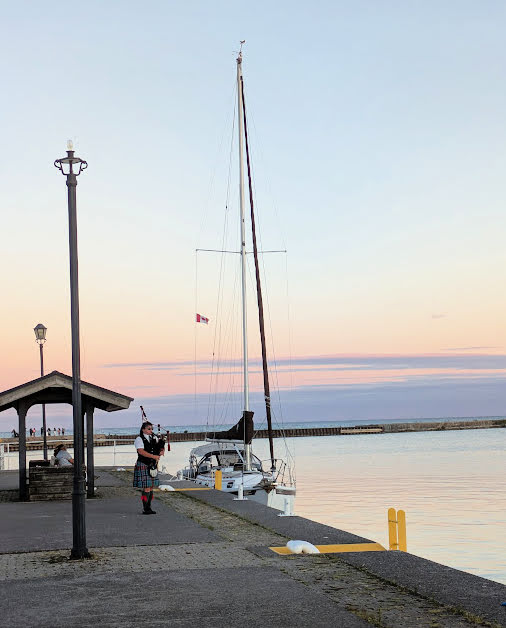 bagpipe player on the dock next to sailboat at sunset 
