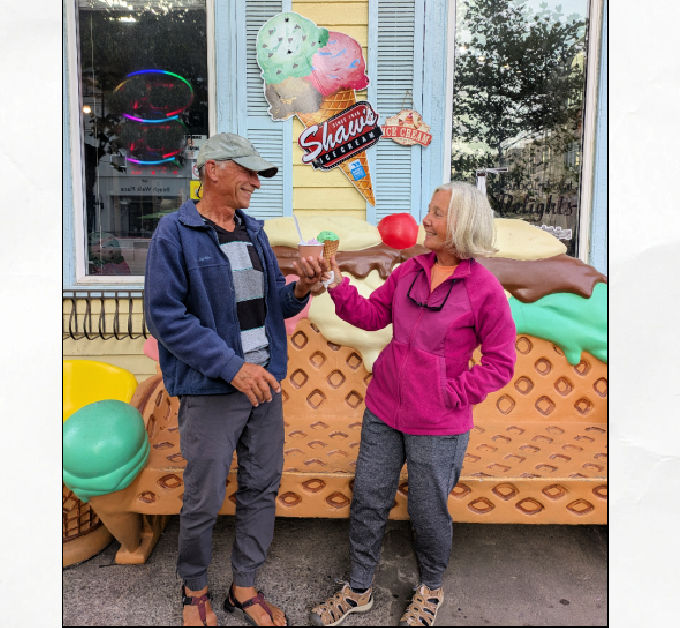 couple eating ice cream in front of ice cream store and bench 
