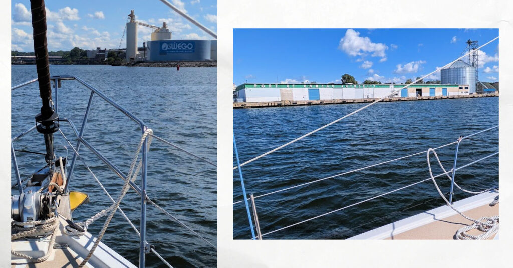 sailboat entering port of oswego with commercial buildings on shore 
