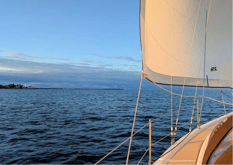 headsail on bow of boat, point of land in distance, mostly blue sky