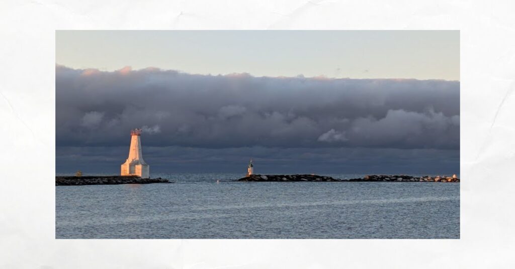 dark clouds in sky outside cobourg harbor entrance marked with lighthouse and breakwaters
